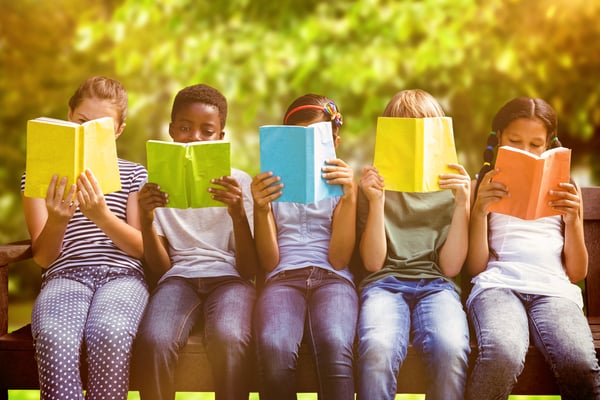 Children reading books at park against trees and meadow in the park