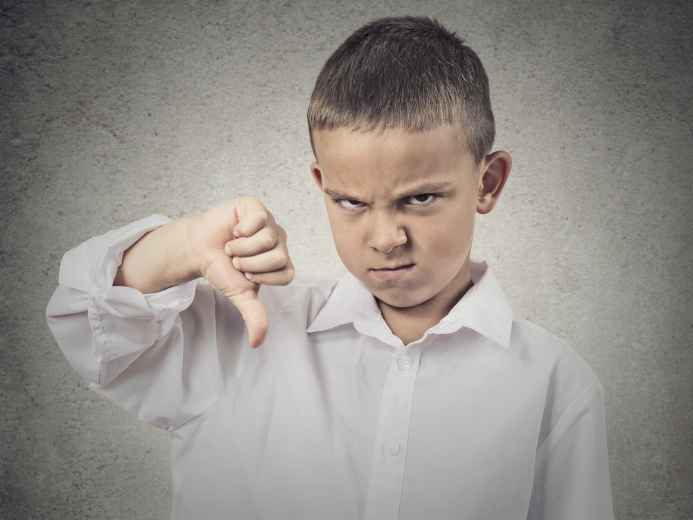 Portrait unhappy, Angry, Displeased Child giving Thumbs Down hand gesture, isolated grey wall background. Negative human Face Expressions, Emotions, Feelings, attitude, life perception, body language
