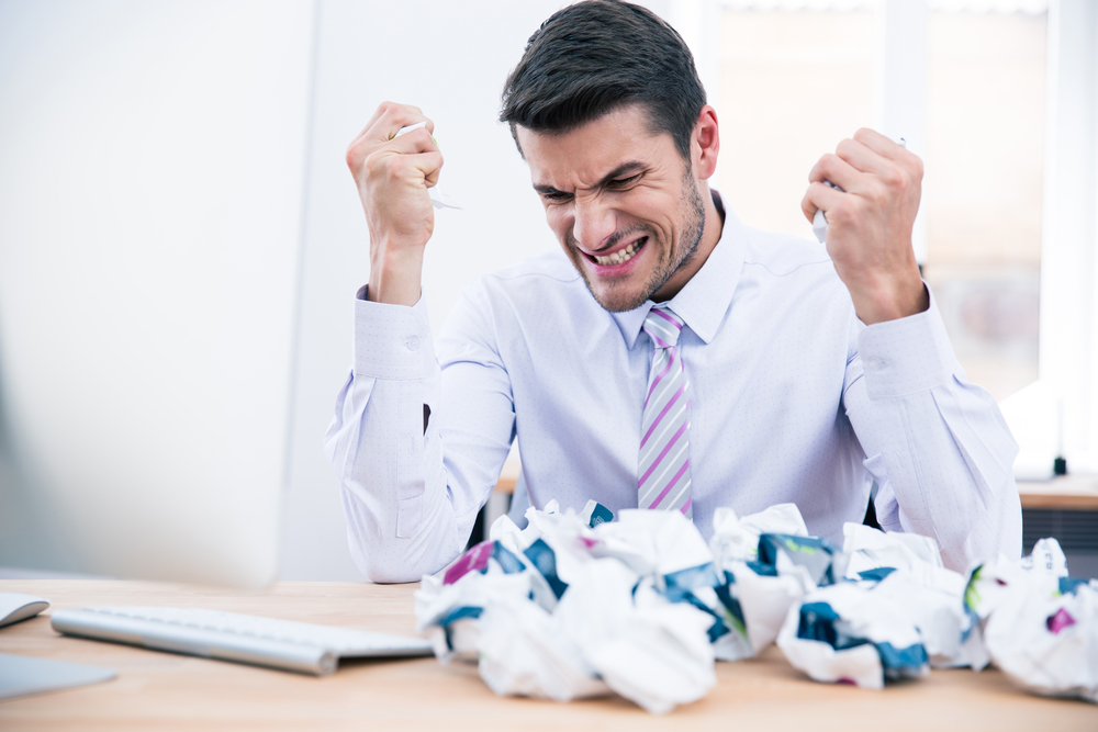 Upset businessman sitting at the table with crumpled paper in office